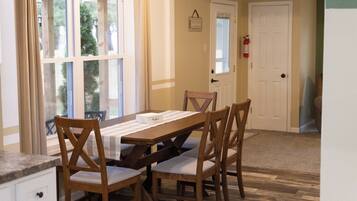 Un comedor con una mesa de madera, cuatro sillas y un ventanal con cortinas.