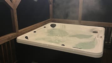 Un jacuzzi con escalones de acceso, rodeado de cubiertas de madera y un techo de madera.