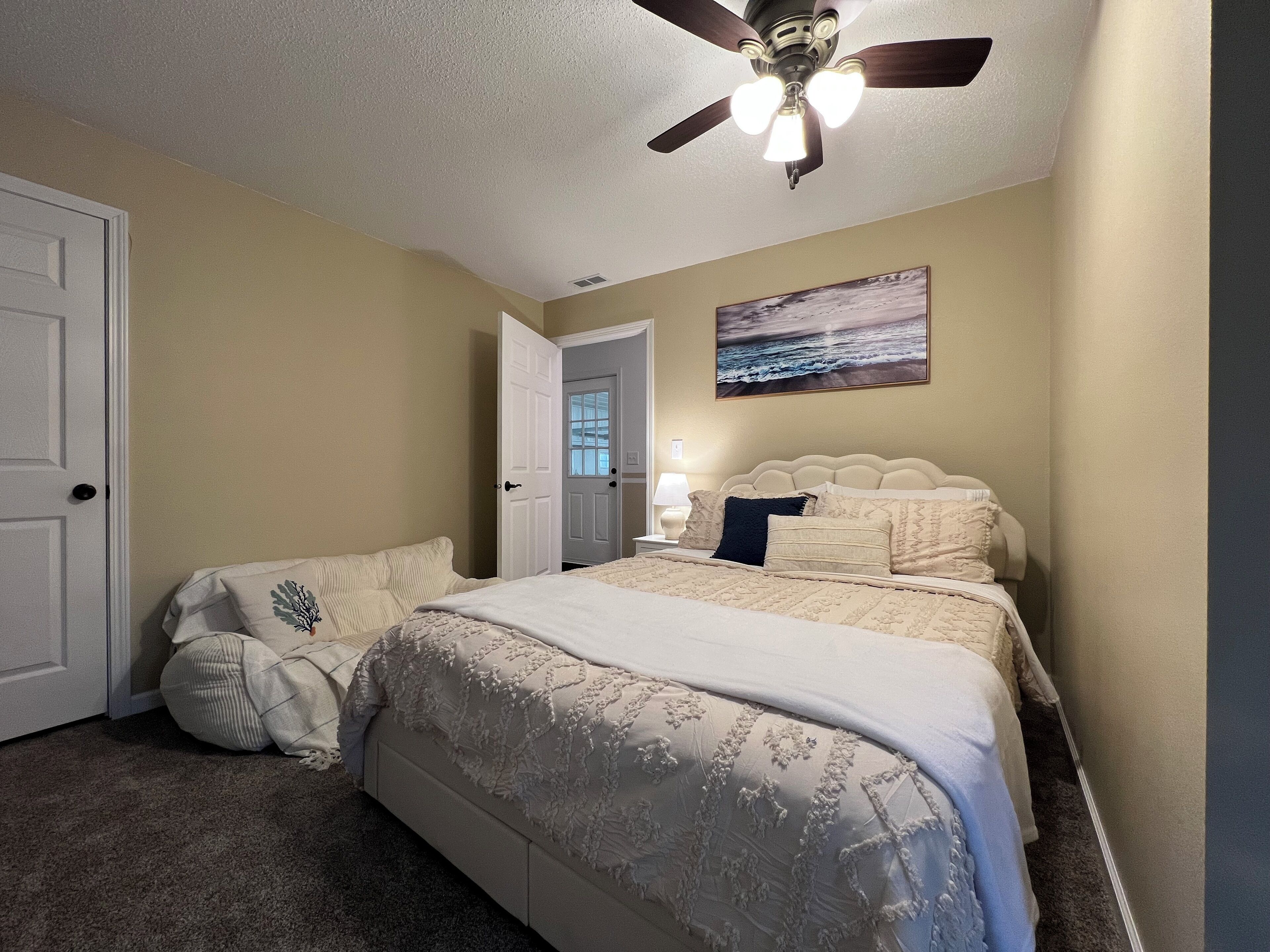 A bedroom with a bed, a ceiling fan, a door, and a painting on the wall.