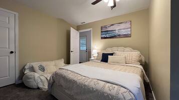 A bedroom with a bed, a ceiling fan, a door, and a painting on the wall.