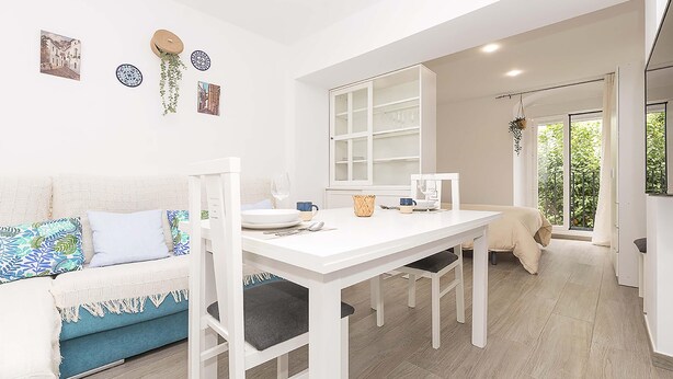 Een moderne, goed verlichte kamer met een witte eettafel, stoelen en een blauwe bank met gestreepte kussens.