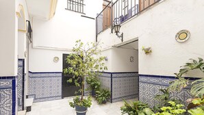 Een binnenplaats met betegelde vloer, plantenbakken en een witte muur met blauwe decoratieve tegels.