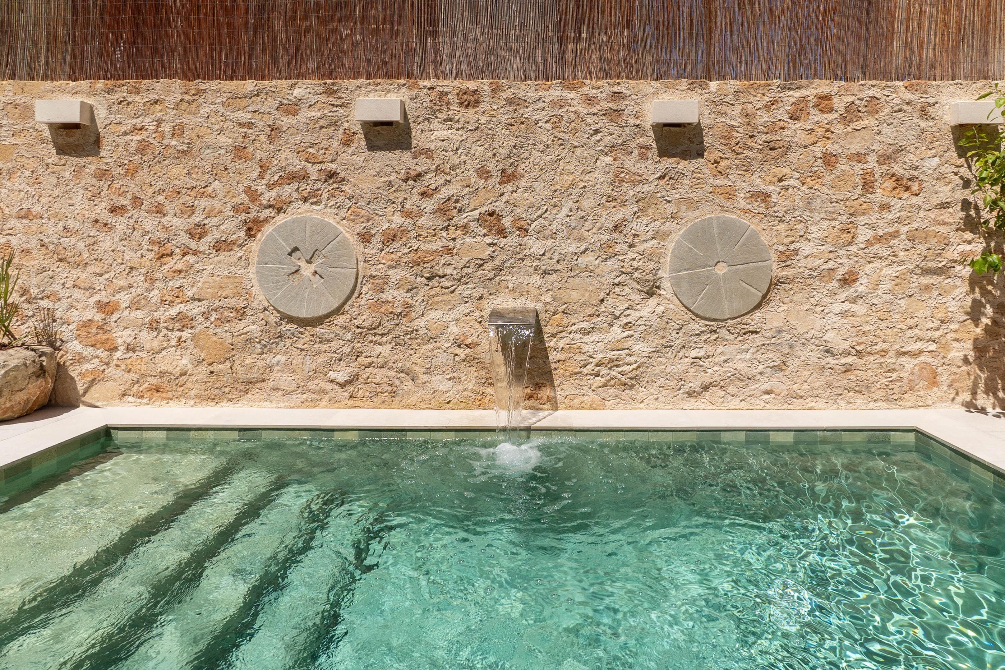 Una piscina con un muro de piedra y dos estructuras circulares de piedra.