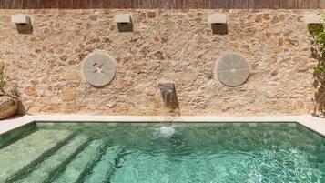 Una piscina con un muro de piedra y dos estructuras circulares de piedra.