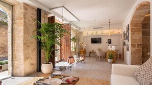 A modern living room with a large window, a coffee table, a sofa, and a dining area with chairs and a table. - VILA NOVA SUITES & SPA - DOBLE DELUXE CON BALCÓN (Capdepera)