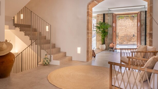 A modern interior with a staircase, a round rug, and a seating area with a view of an outdoor stone wall. - VILA NOVA SUITES & SPA - DOBLE DELUXE CON BALCÓN (Capdepera)