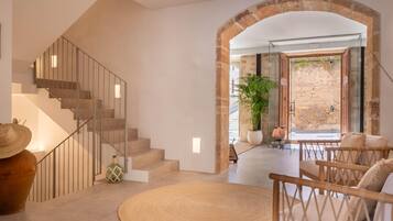 Un interior moderno con una escalera, un tapete redondo y una zona de estar con vista a una pared de piedra exterior.