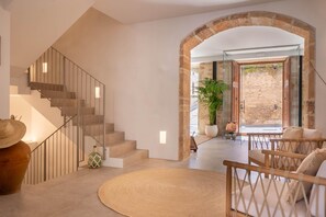 A modern interior with a staircase, a round rug, and a seating area with a view of an outdoor stone wall. - VILA NOVA SUITES & SPA - DOBLE DELUXE CON BALCÓN (Capdepera)