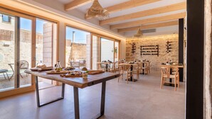 Un vaste espace dédié à la salle à manger, doté de grandes fenêtres, de poutres en bois et d’un mur en pierre rustique.