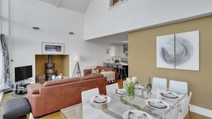 Un salón espacioso con chimenea, una mesa de comedor para cuatro personas y una cocina moderna al fondo.