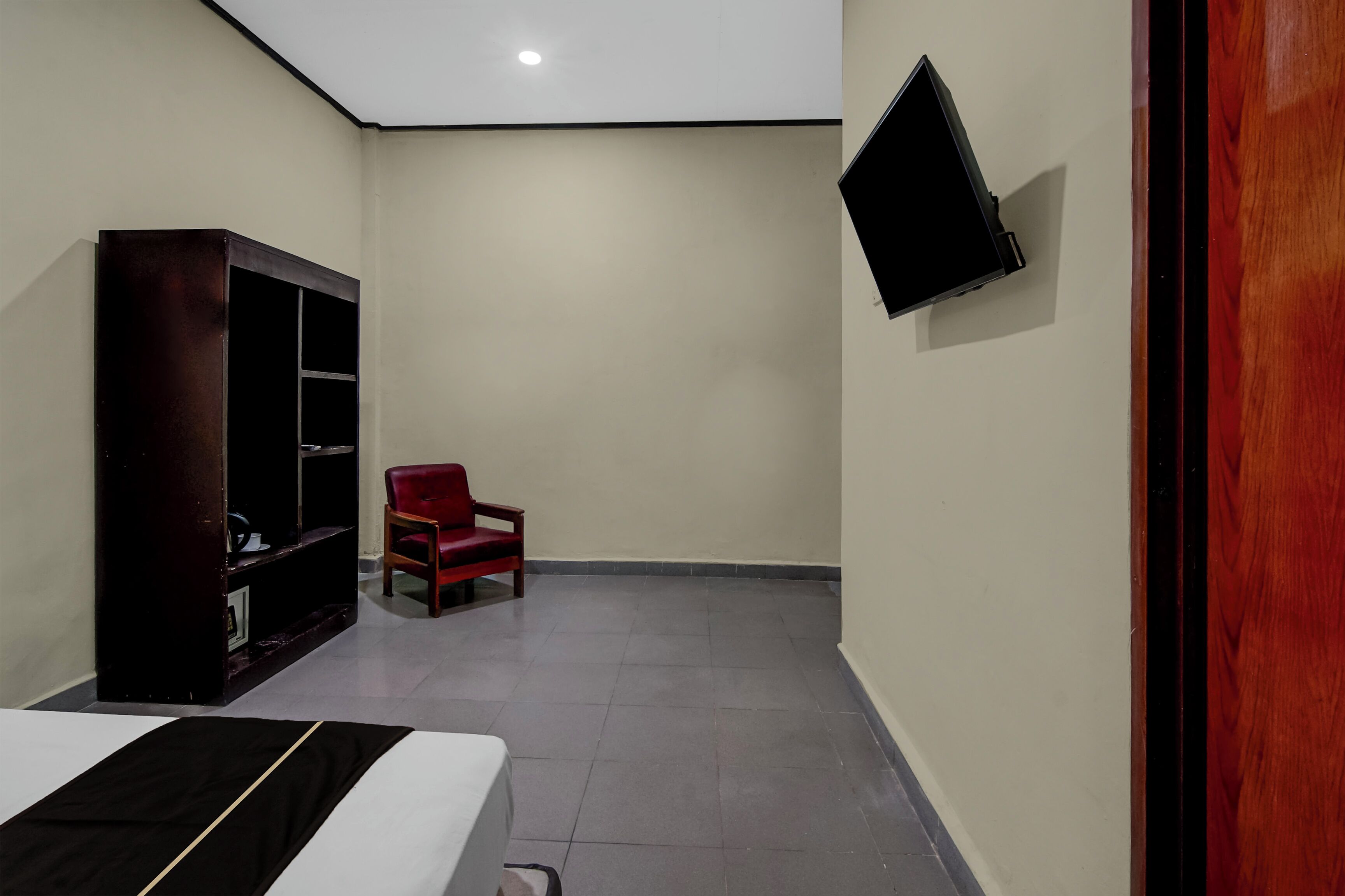 Een kamer met een bed, een rode stoel, een aan de muur bevestigde televisie en een kledingkast.