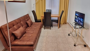 A furnished room with a brown leather sofa, a dining table with chairs, a TV on a stand, and a floor lamp. - Happy House Central Apartment (Faro)