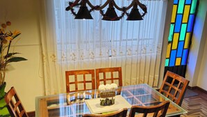 Un espace repas avec une table en verre, des chaises en bois et un luminaire décoratif suspendu au plafond.