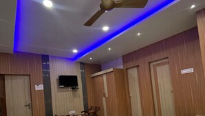 A hotel room with a bed, a desk with a chair, a ceiling fan, and wooden paneling.