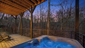 Un jacuzzi bajo una pérgola de madera con vistas a árboles sin hojas y un cielo crepuscular.