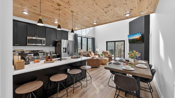 Una cocina moderna con una isla central, taburetes de bar y una zona de comedor con mesa y sillas de madera.