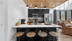 Una cocina moderna con gabinetes negros, una isla central con taburetes y una zona de comedor con sofá.