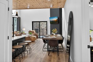 A modern kitchen with a dining area, wooden flooring, and a large TV mounted on the wall. - Modern Smoky Escape - Private Pool and Hot Tub (Sevierville)