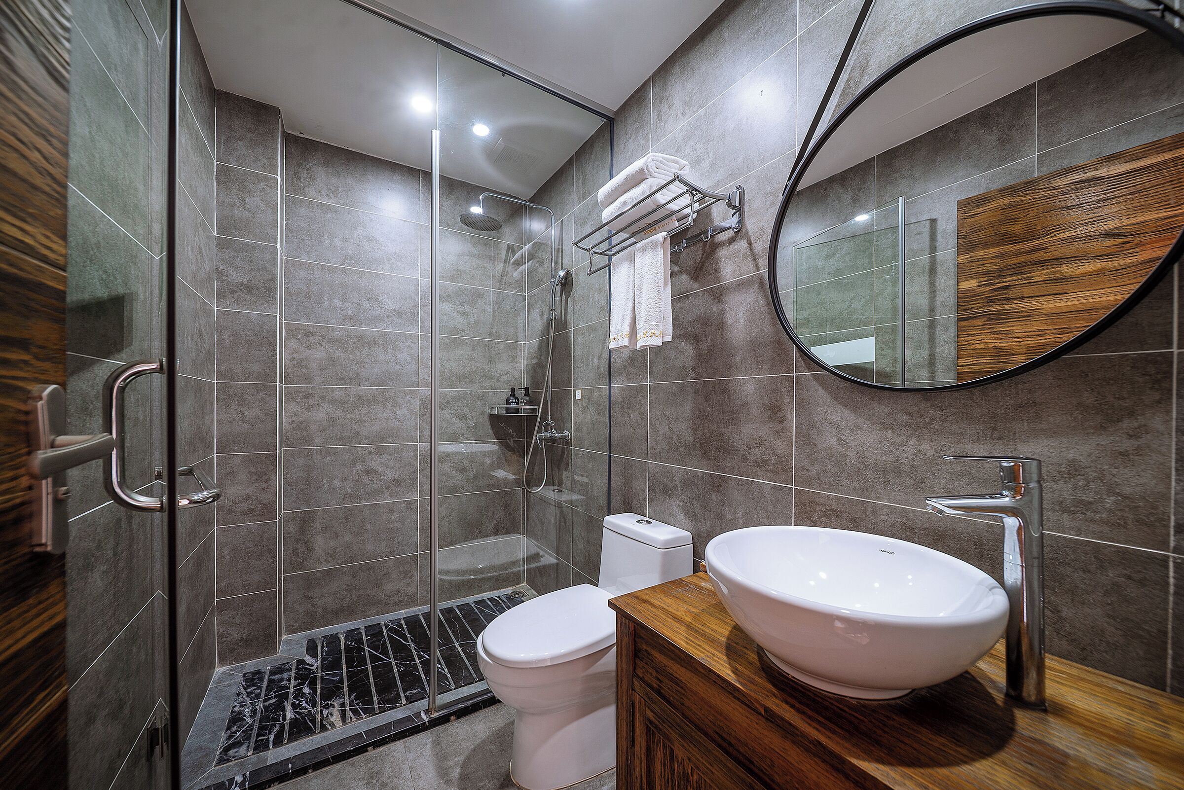 Un baño moderno con ducha de vidrio, inodoro blanco y tocador de madera con lavamanos grande.
