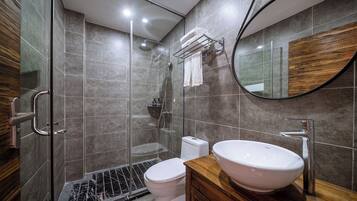 Un baño moderno con ducha de vidrio, inodoro blanco y tocador de madera con lavamanos grande.