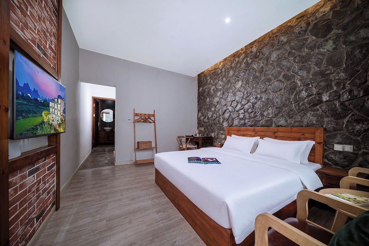 Habitación de hotel con cama, cabecero de madera, pared de piedra y televisor en la pared.