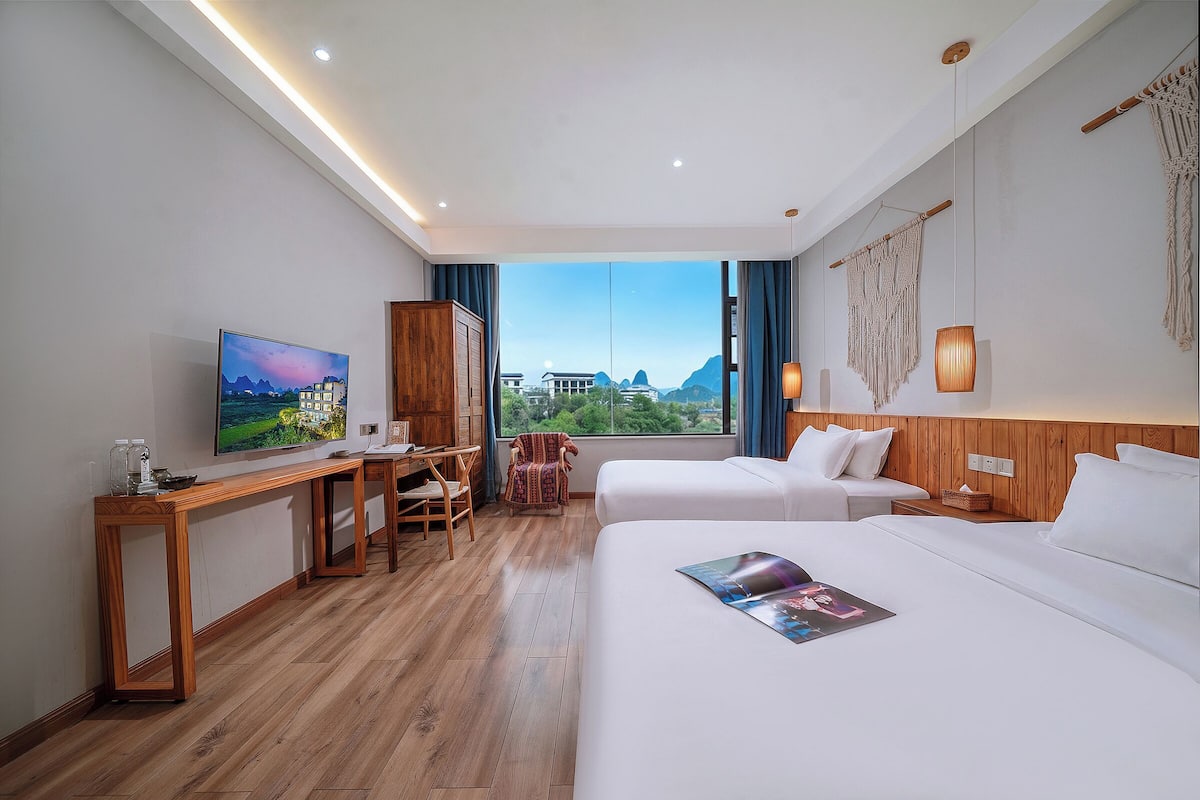 Habitación de hotel con cama, escritorio, silla, televisor y vistas a las montañas.