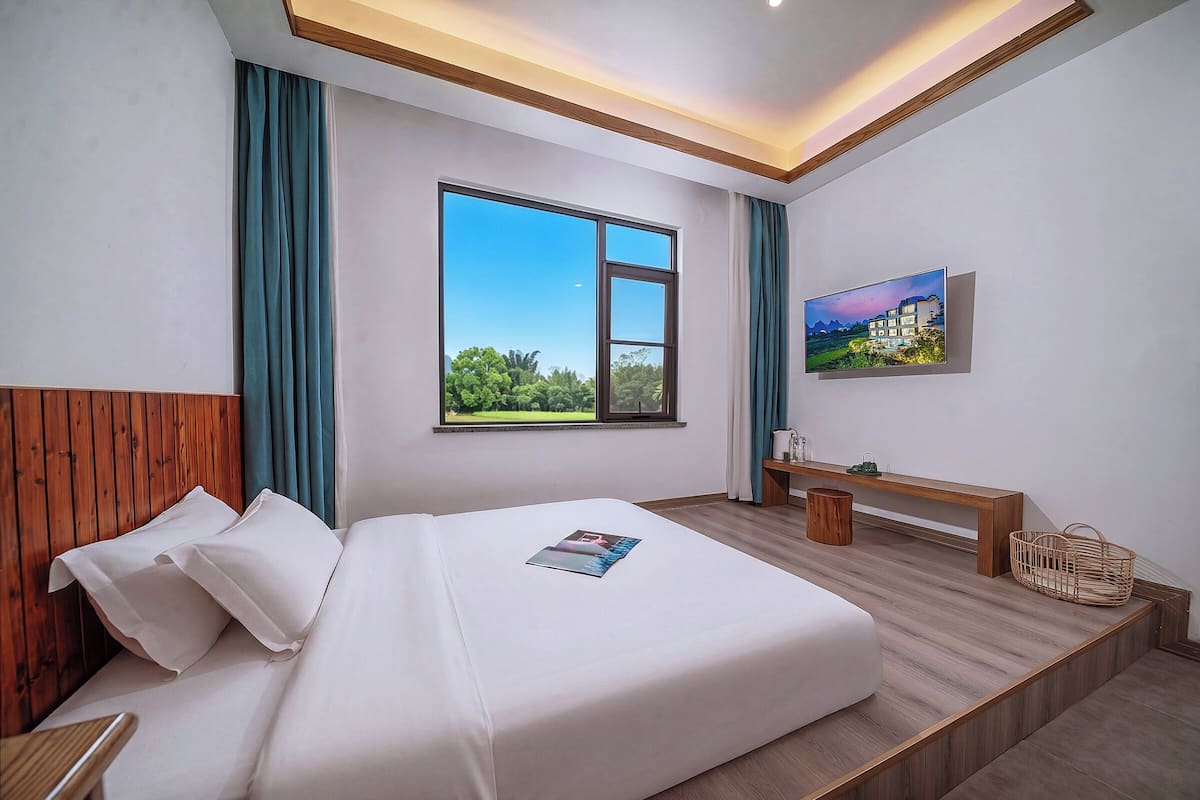 Habitación de hotel moderna con una cama grande, cabecera de madera, ventana con vistas, mesita de noche y un cuadro en la pared.