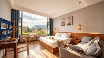 A hotel room with a bed, a sofa, a desk with a computer, and a view of mountains.