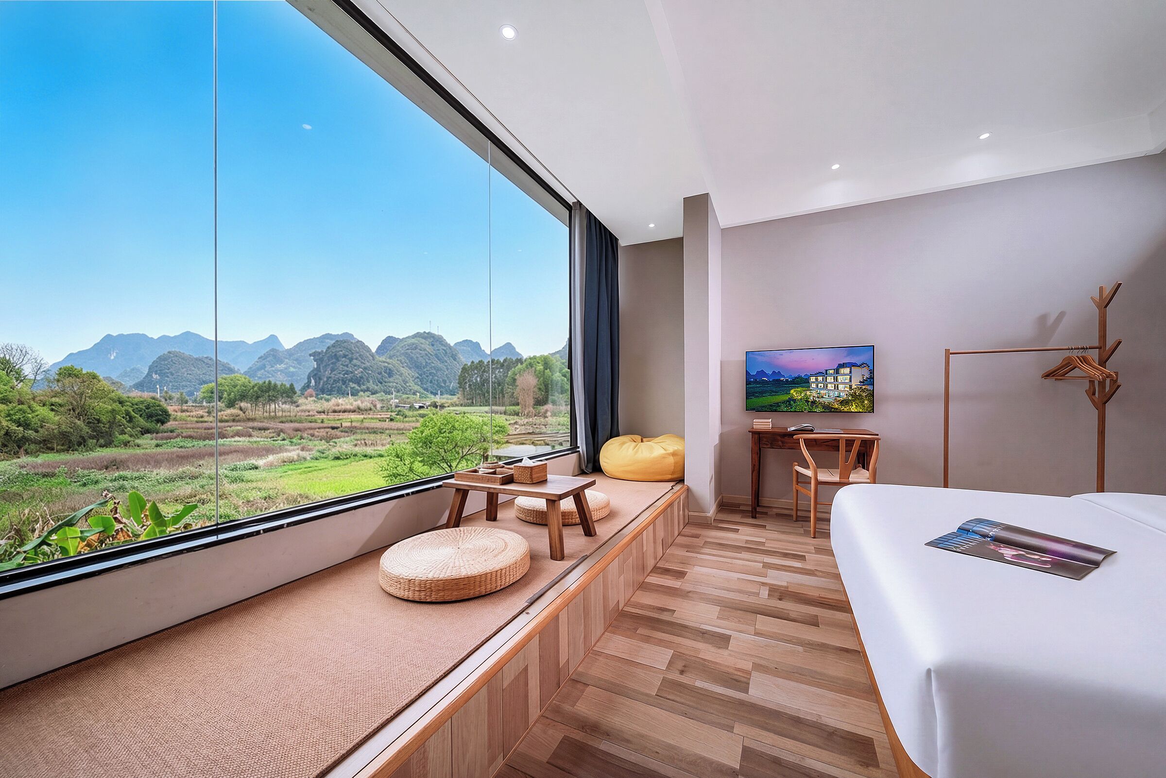 Habitación de hotel moderna con un ventanal grande, suelo de madera, una cama, un escritorio y una silla.