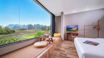 Habitación de hotel moderna con un ventanal grande, suelo de madera, una cama, un escritorio y una silla.