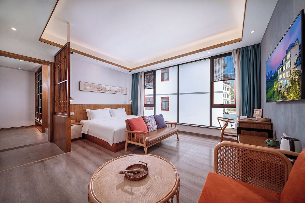 Una habitación de hotel con cama, sofá, mesa de comedor y un amplio ventanal.