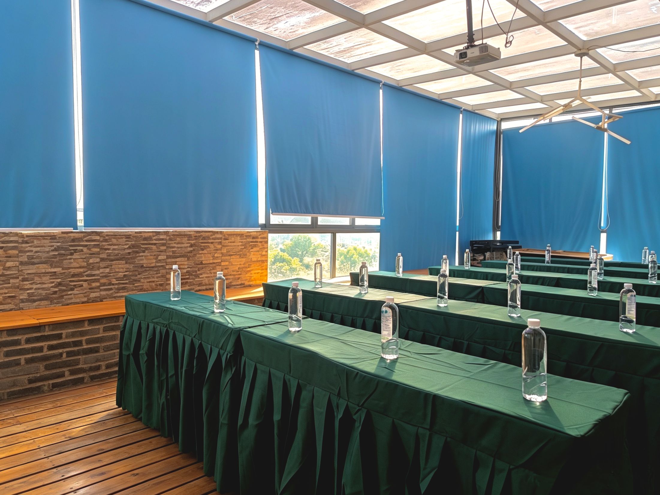 A conference room with tables covered in green cloths, each with a clear bottle. The room has a wooden floor, blue walls, and a brick accent wall.