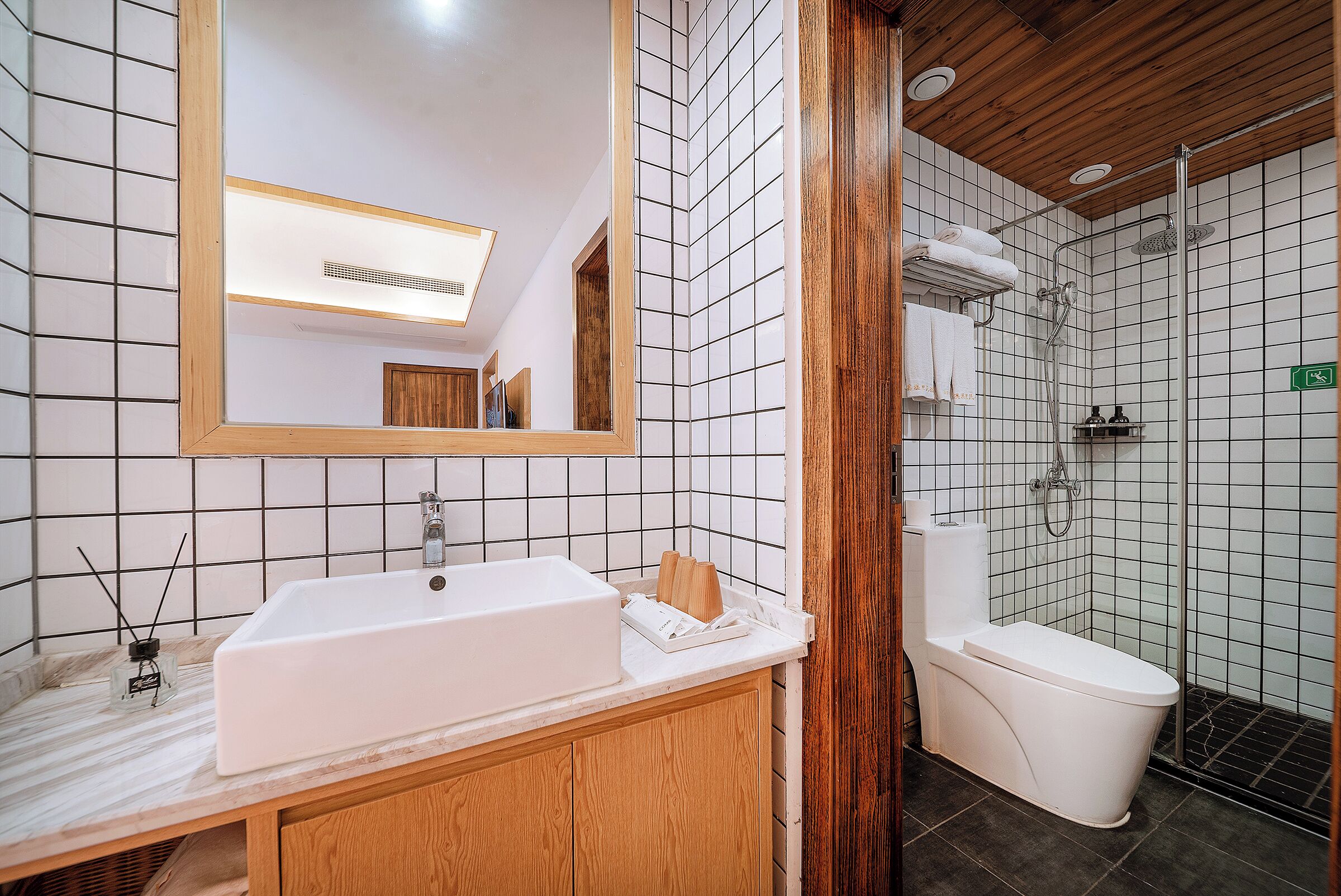 Ein Badezimmer mit einem weißen Waschbecken, Holzschränken, einem Spiegel, einer Dusche und einer Toilette.