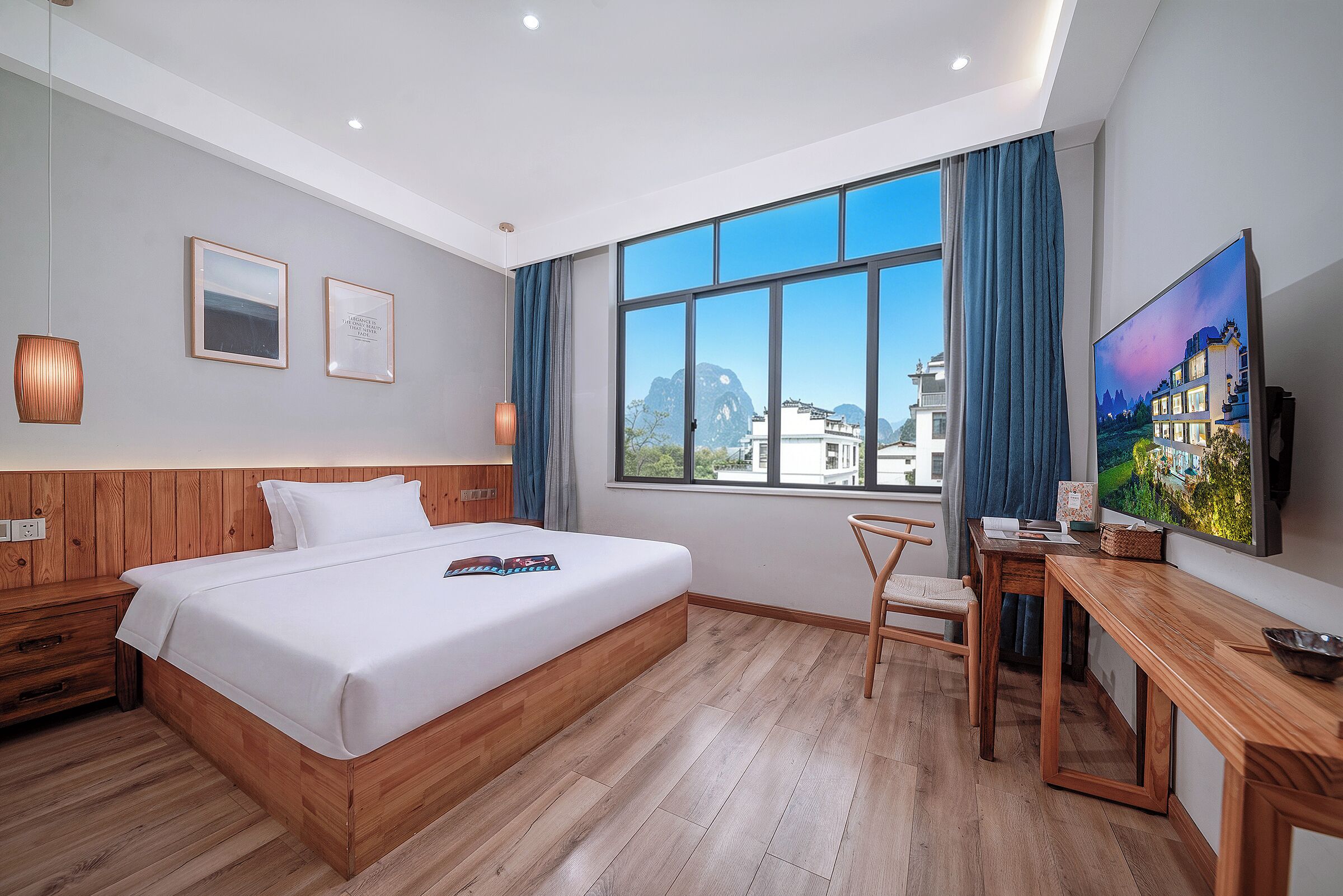 A modern hotel room with a large bed, wooden flooring, a desk, and a TV.