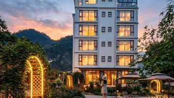 A multi-story hotel with a pool, surrounded by lush greenery and a mountainous backdrop.