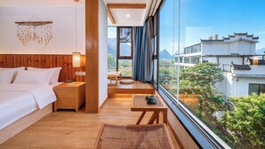 Un dormitorio con cama, mesita de noche y vistas de la ciudad a través de amplias ventanas.