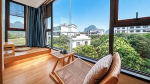 Una habitación moderna con ventanas amplias, un banco de madera, una pequeña mesa y vistas a edificios y vegetación.