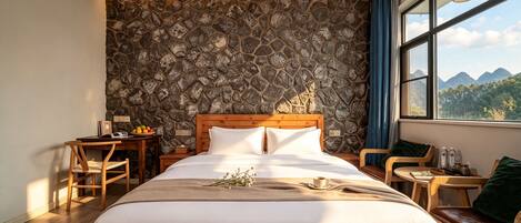 Habitación de hotel con pared de piedra, cama de madera, escritorio y vistas a las montañas.