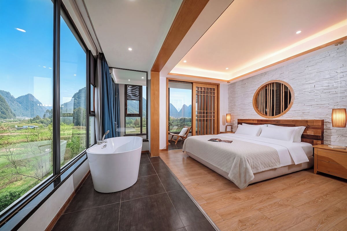 Un dormitorio moderno con un ventanal grande, una bañera, una cama y vistas a un paisaje montañoso.