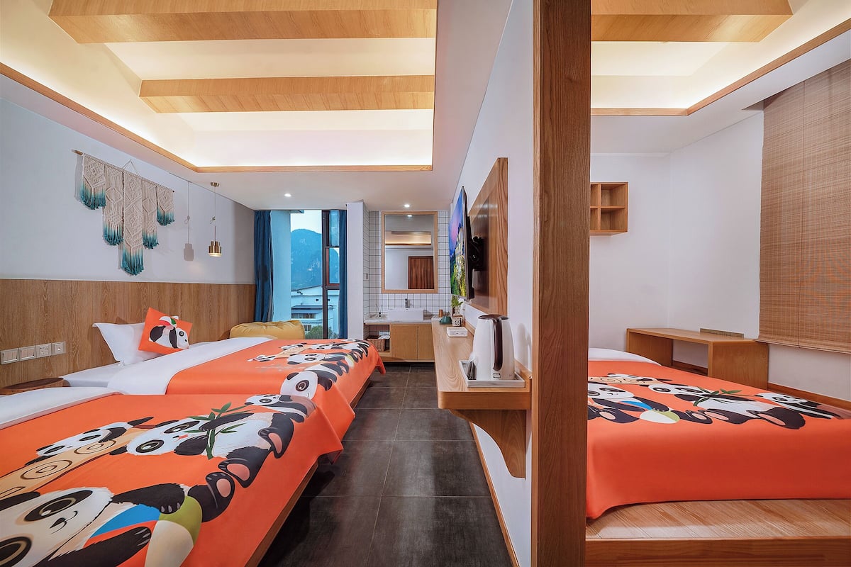 Habitación de hotel con dos camas, kitchenette, televisor y un amplio ventanal.
