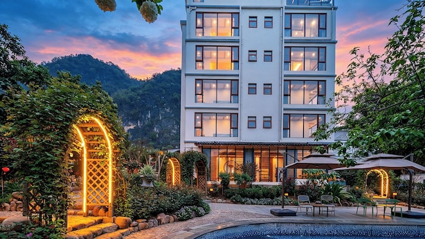 Un hotel de varios pisos con un patio jardín, mobiliario exterior y una piscina.