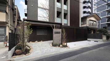A modern building with a stone-paved entrance, a gated driveway, and a sign indicating it's a residential area.