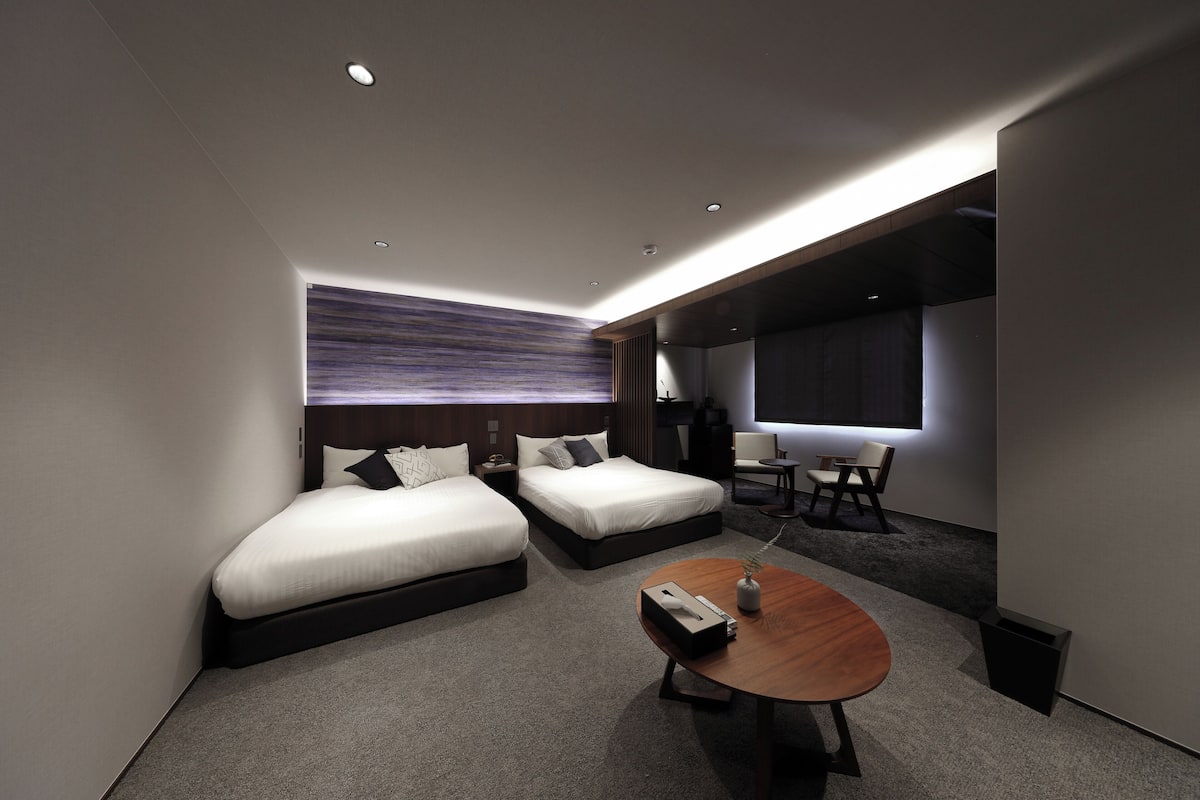 A modern hotel room with two beds, a small table, and a large window.
