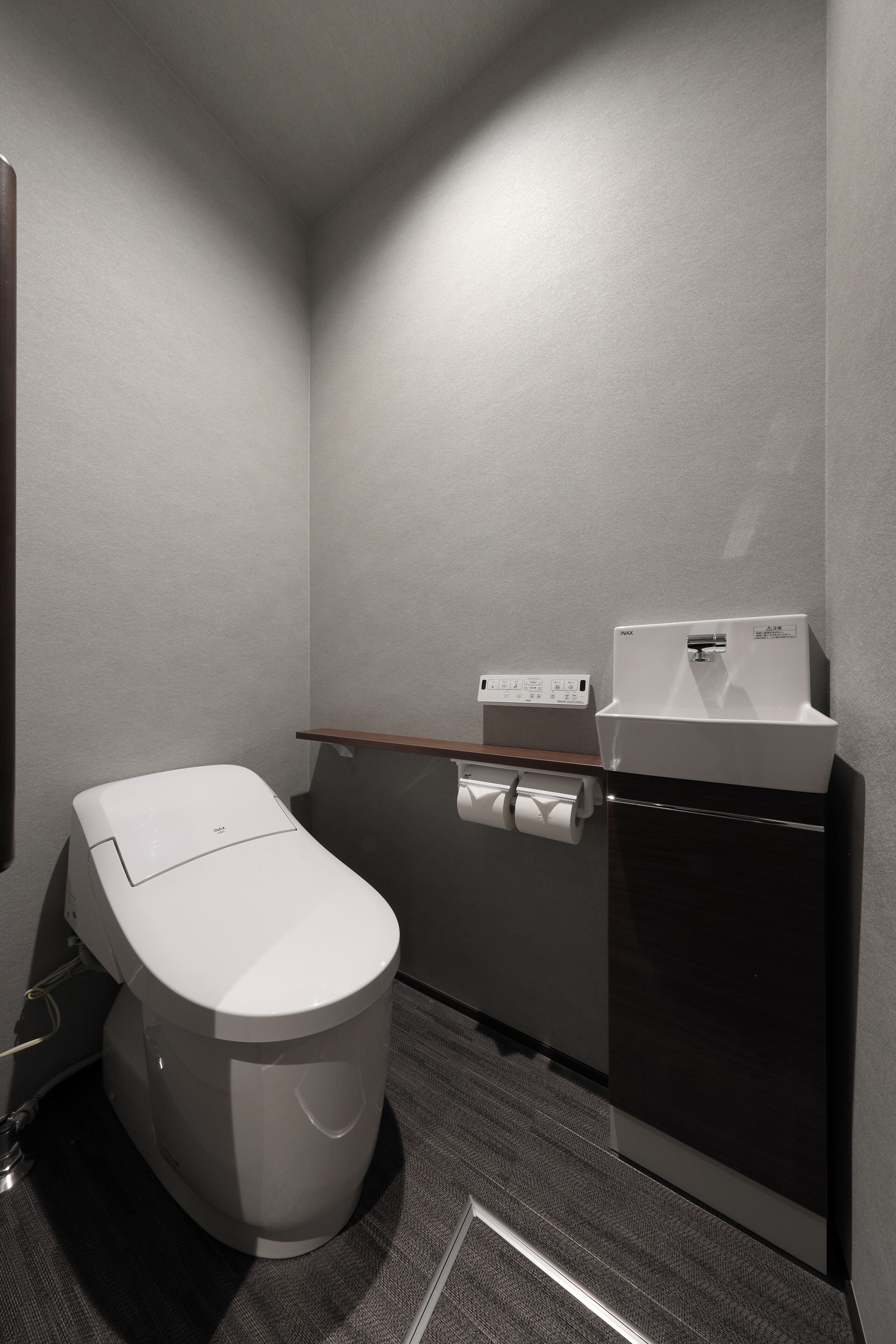 Un baño pequeño y moderno con inodoro, secamanos y dispensador de toallas de papel.