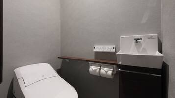 Une petite salle de bain moderne équipée de toilettes, d’un sèche-mains et d’un distributeur de serviettes en papier.