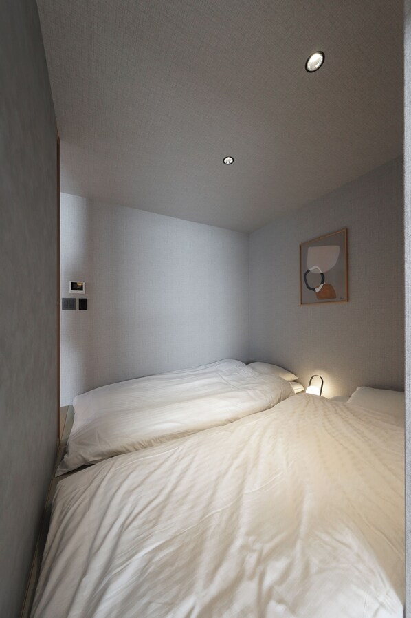 A small, single-bed room with a plain wall, a ceiling light, and a framed picture. - GRACE STAY Hiroshima Peace Memorial Park (Hiroshima)