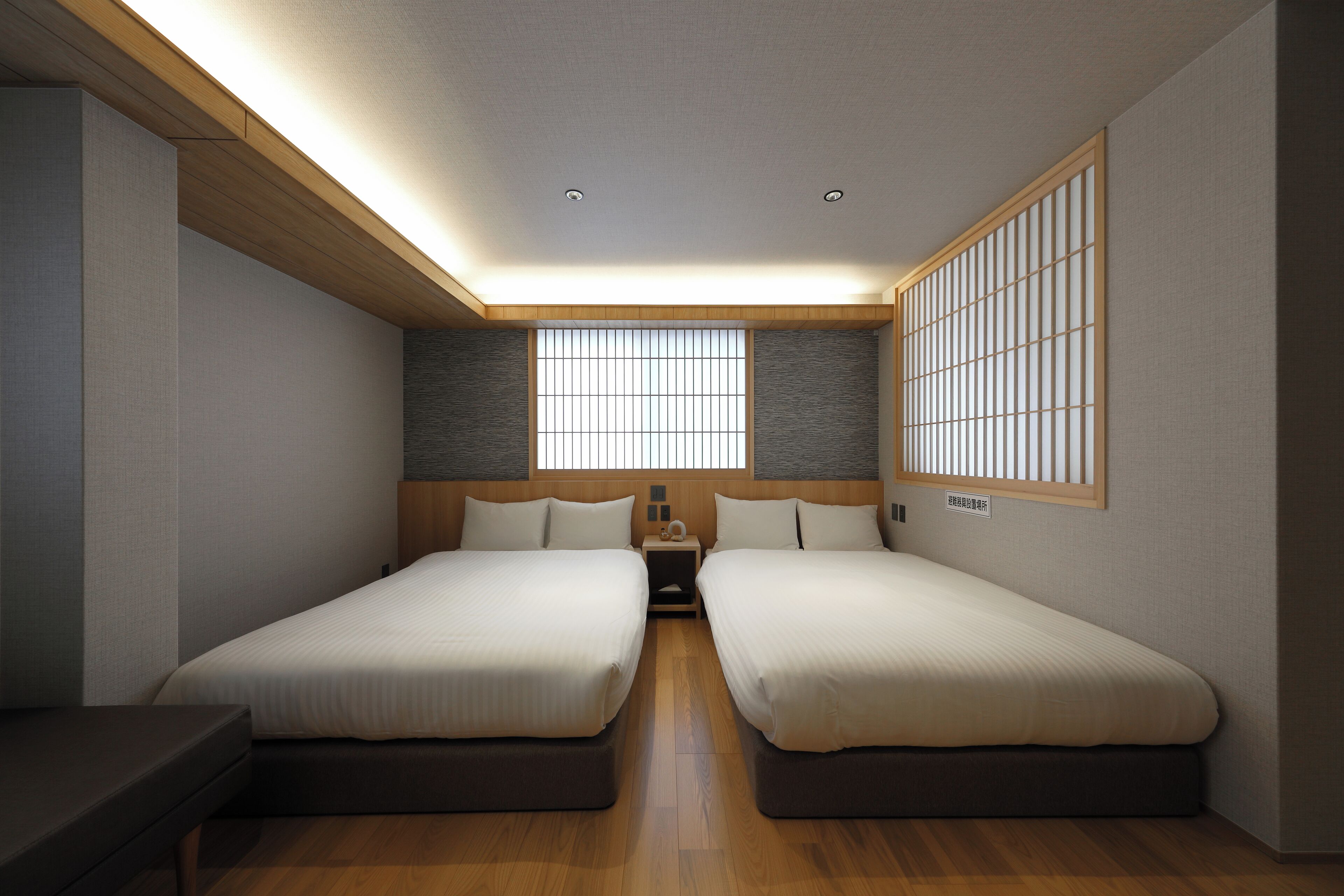 A modern hotel room with two beds, a wooden ceiling, a large window with blinds, and a nightstand with a lamp.