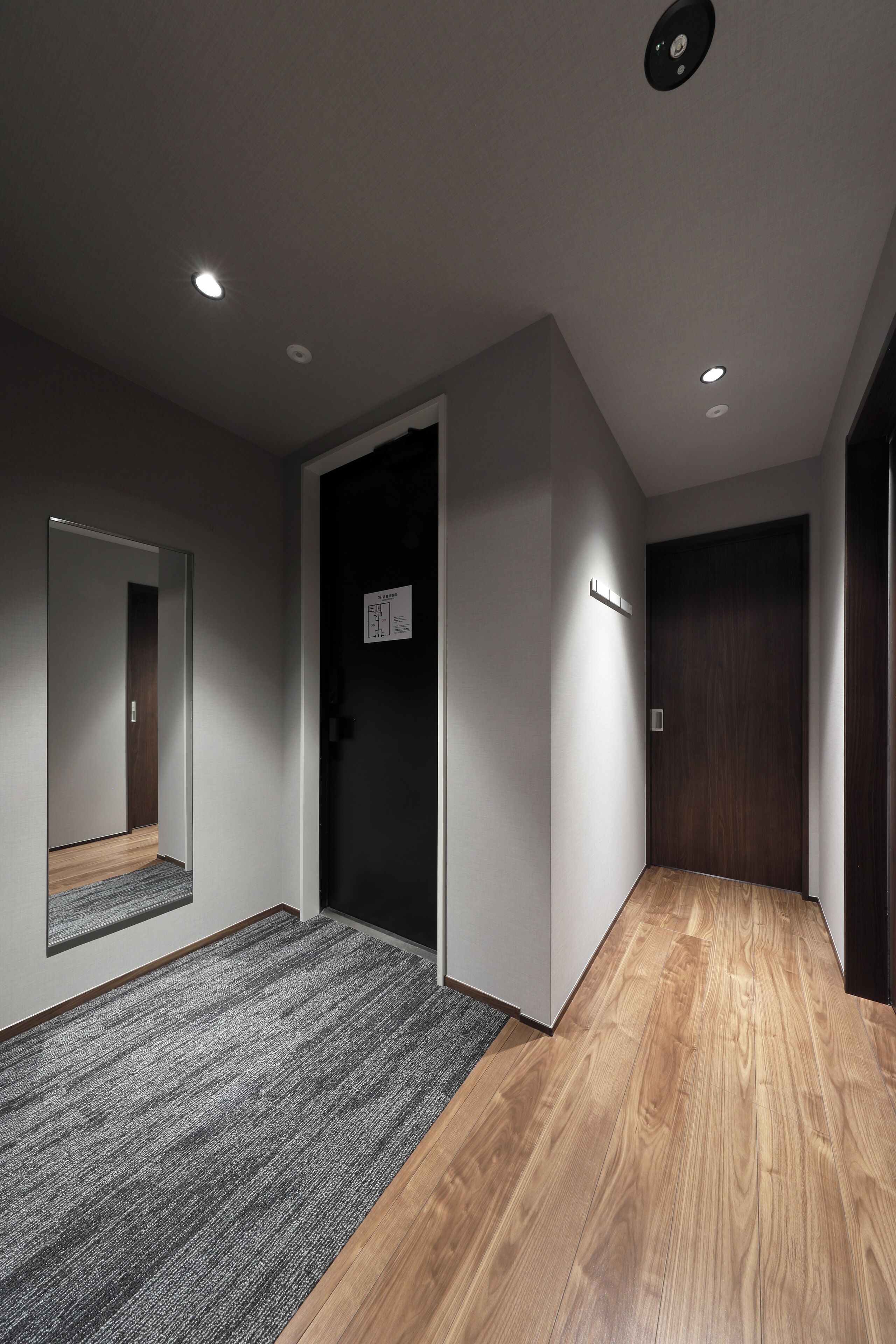 A hallway with a carpeted area and a wooden floor, a door with a sign, and recessed ceiling lighting.