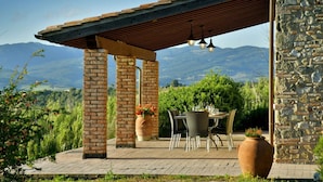 Un área de comedor al aire libre techada, con columnas de ladrillo, una mesa, sillas y plantas en macetas.