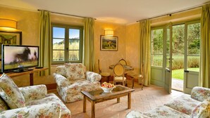 Un salón con tapicería floral, un televisor, una mesa de comedor con sillas y vistas al exterior a través de amplias ventanas.